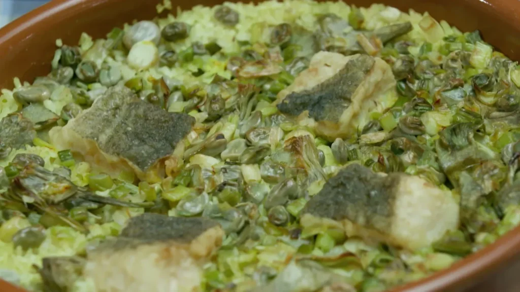 Cassola de Quaresma recien horneada con el arroz las alcachofas y el bacalao dorados en una fuente de barro tradicional