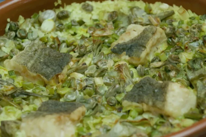 Cassola de Quaresma recien horneada con el arroz las alcachofas y el bacalao dorados en una fuente de barro tradicional