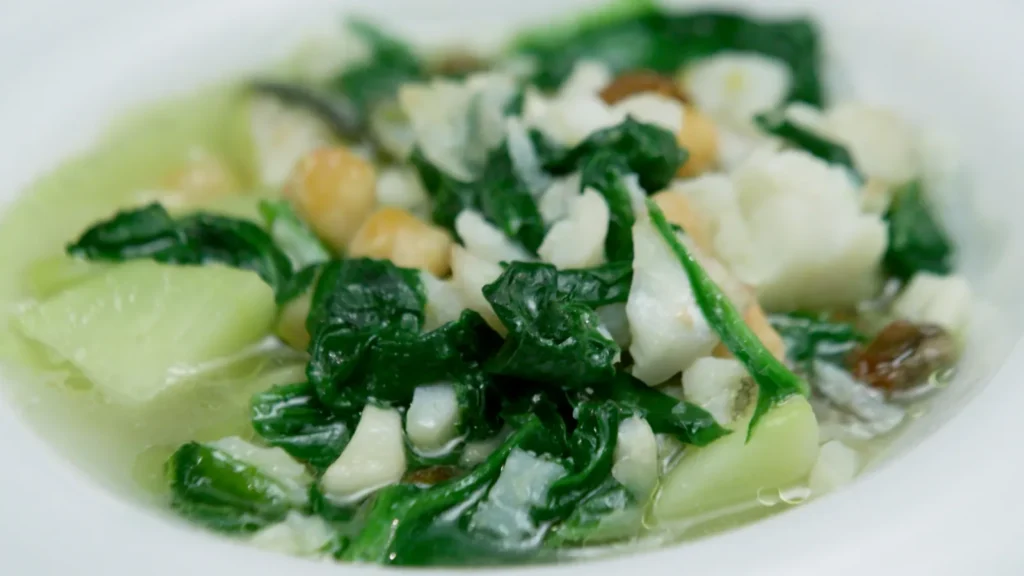 Un plato humeante de potaje de vigilia con sus garbanzos espinacas y bacalao servido en una mesa de madera
