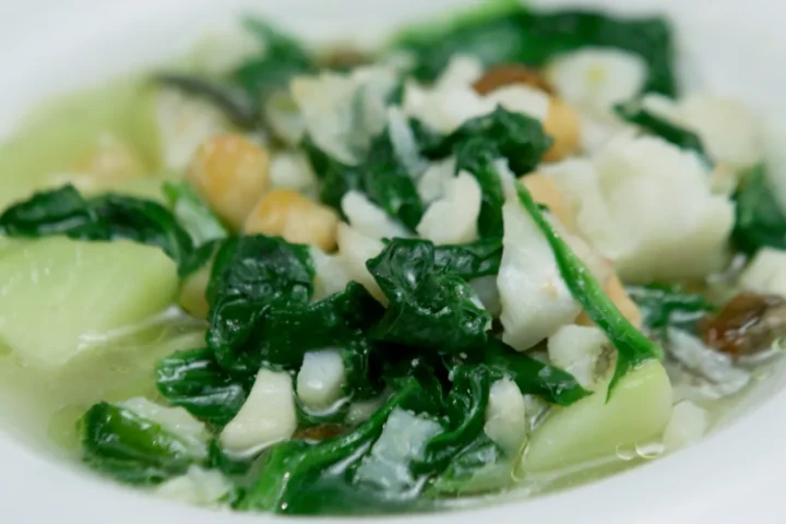 Un plato humeante de potaje de vigilia con sus garbanzos espinacas y bacalao servido en una mesa de madera