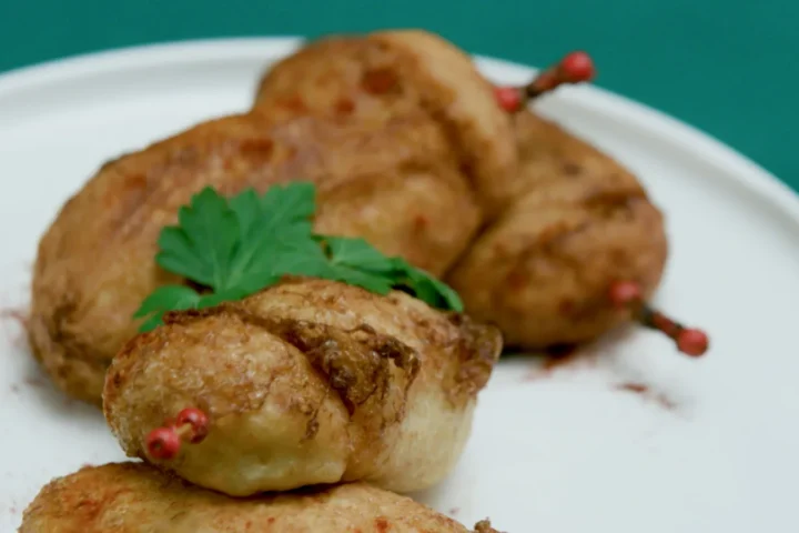 Un plato lleno de ximos dorados y crujientes cortados por la mitad mostrando su jugoso relleno de atun tomate y huevo duro